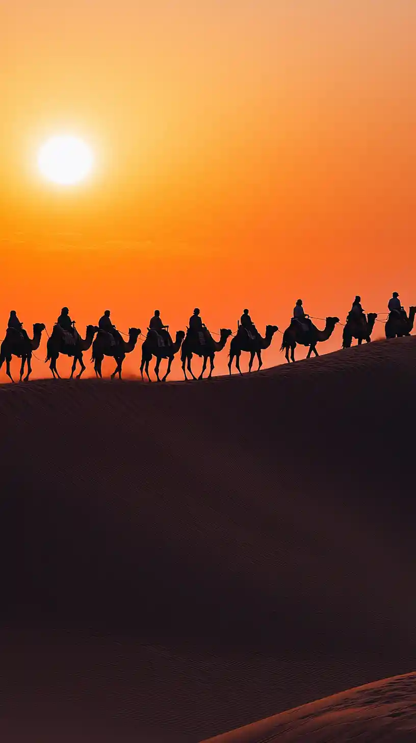 Silhouetted camel caravan crossing dunes at fiery sunset