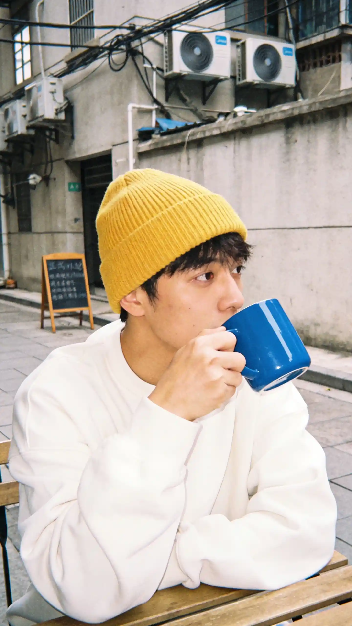 Young man in yellow beanie sipping coffee at city cafe