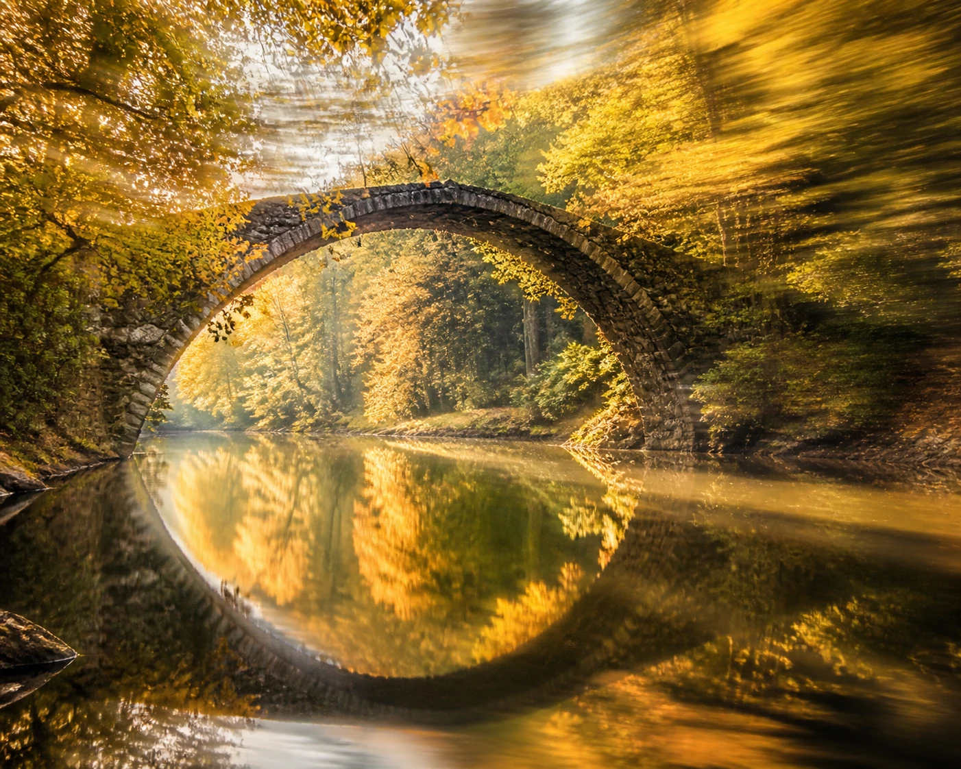 Ancient stone bridge reflecting over a calm autumn river