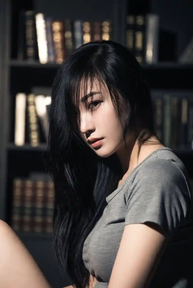 부드러운 빛 속 책장 옆 바닥에 앉아 있는 아시아 여성