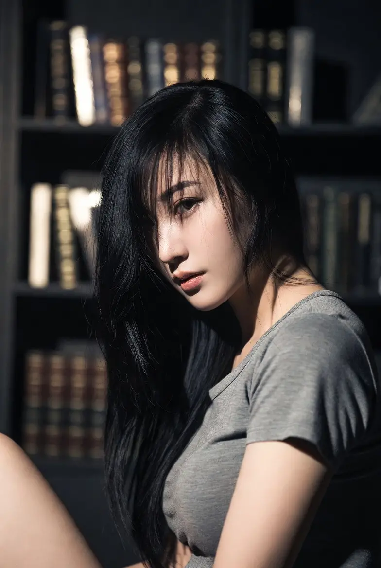 Femme asiatique assise au sol près d’une bibliothèque dans une lumière douce
