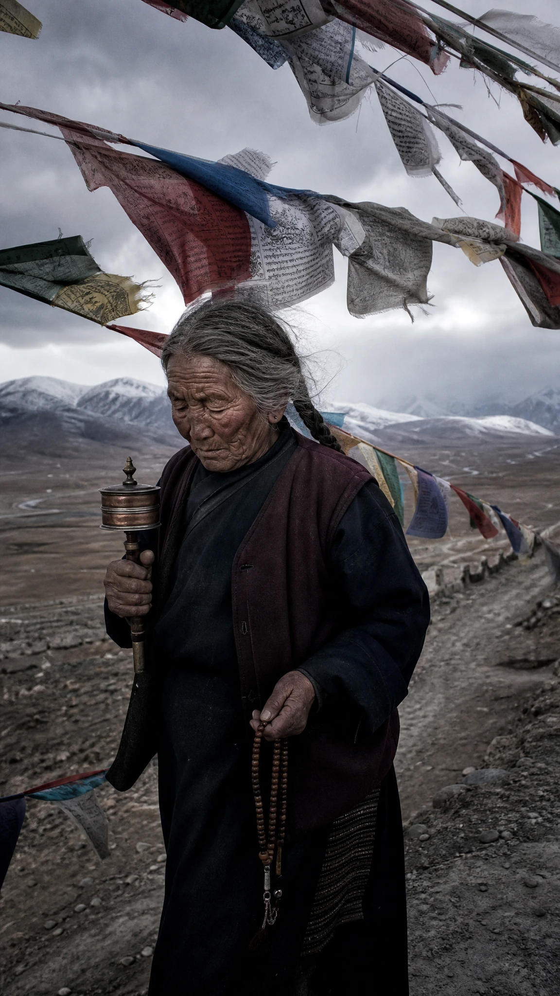 Idosa tibetana caminhando sob bandeiras de oração desgastadas