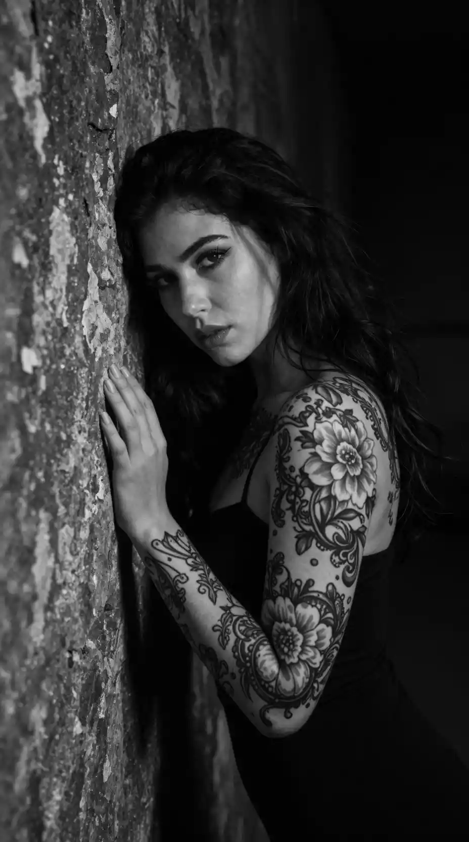 Tattooed woman in moody black and white against stone wall