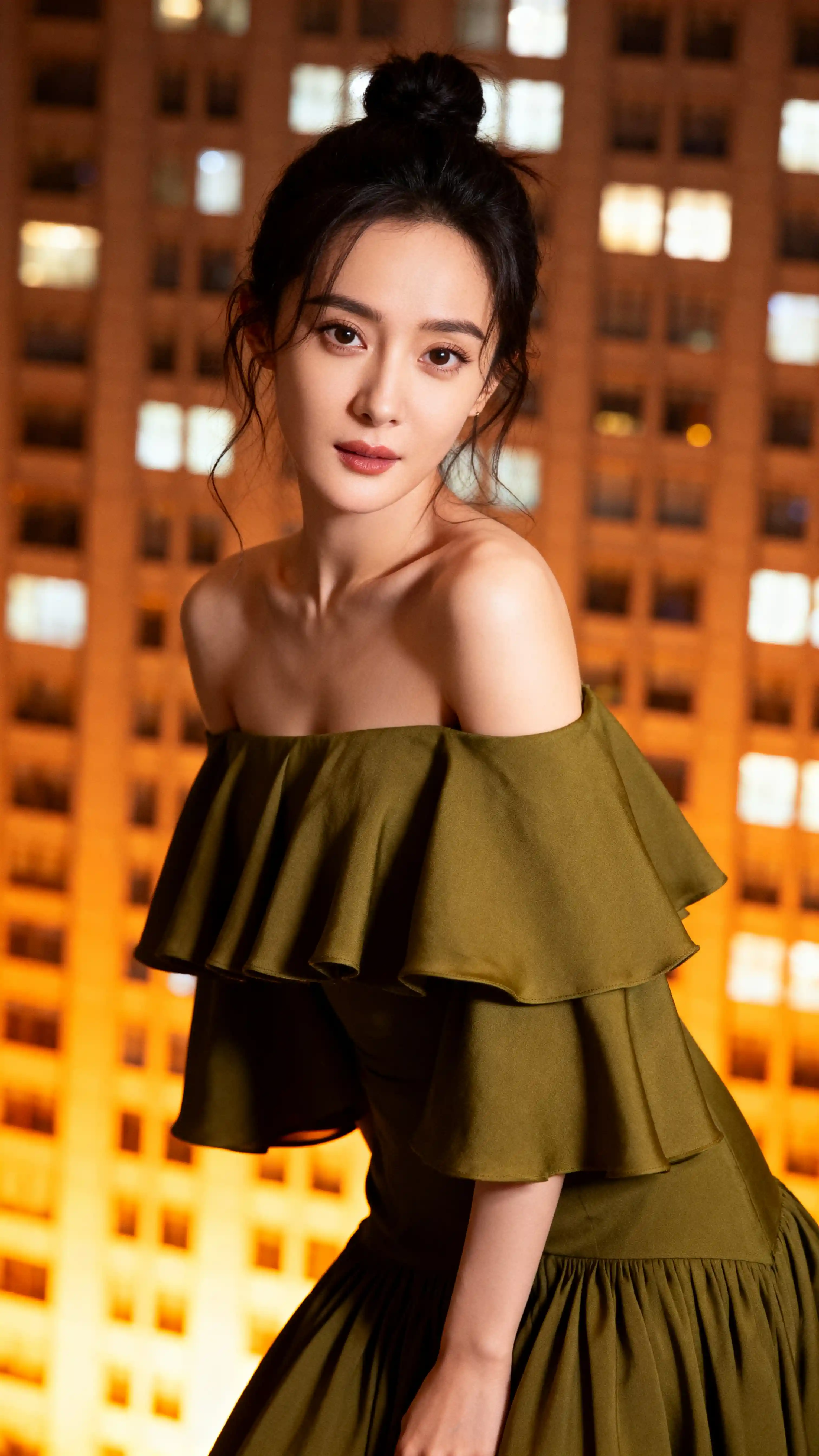 Chic woman posing by urban high rise window at dusk