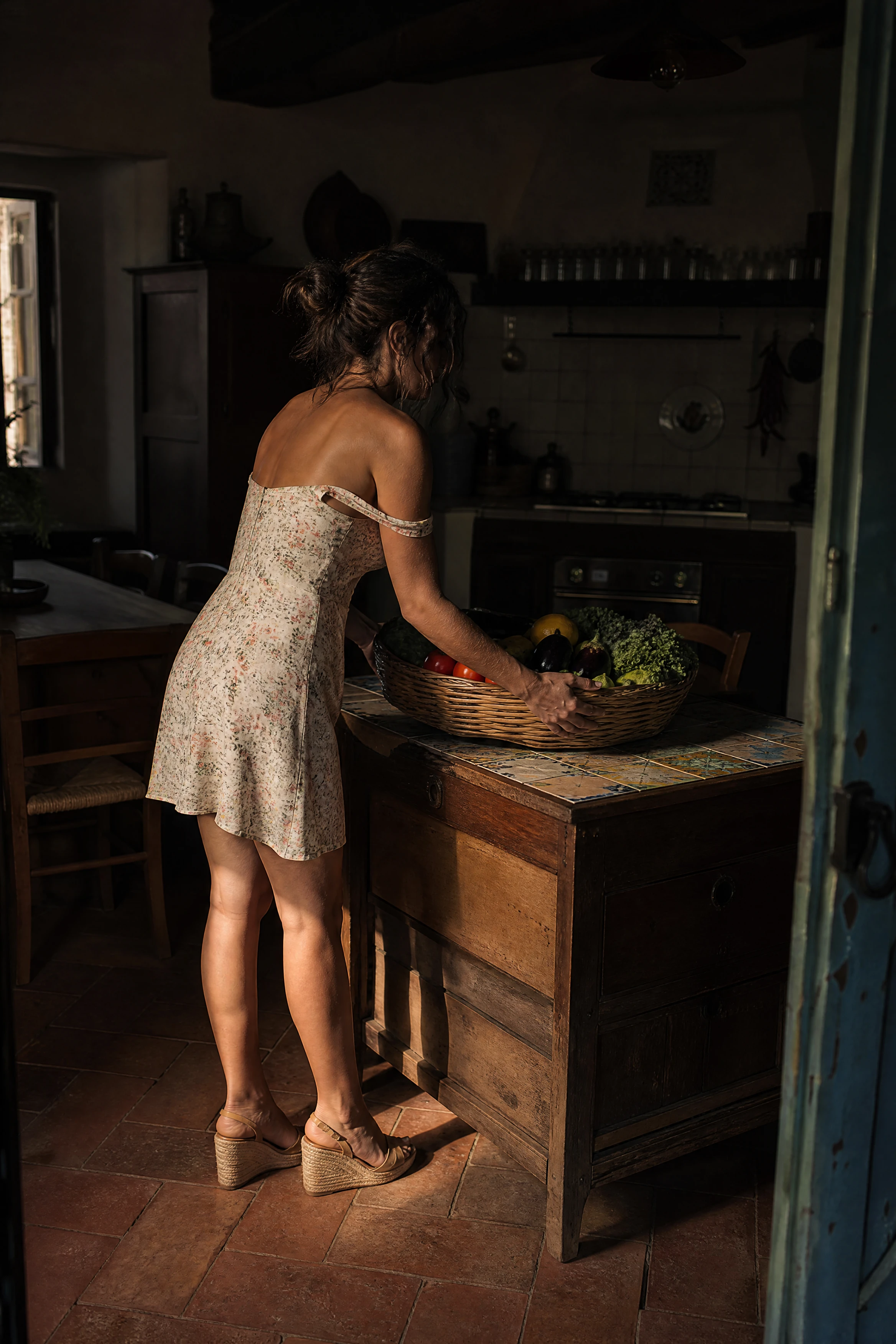Donna italiana che entra in una cucina rustica in penombra con cesto del raccolto