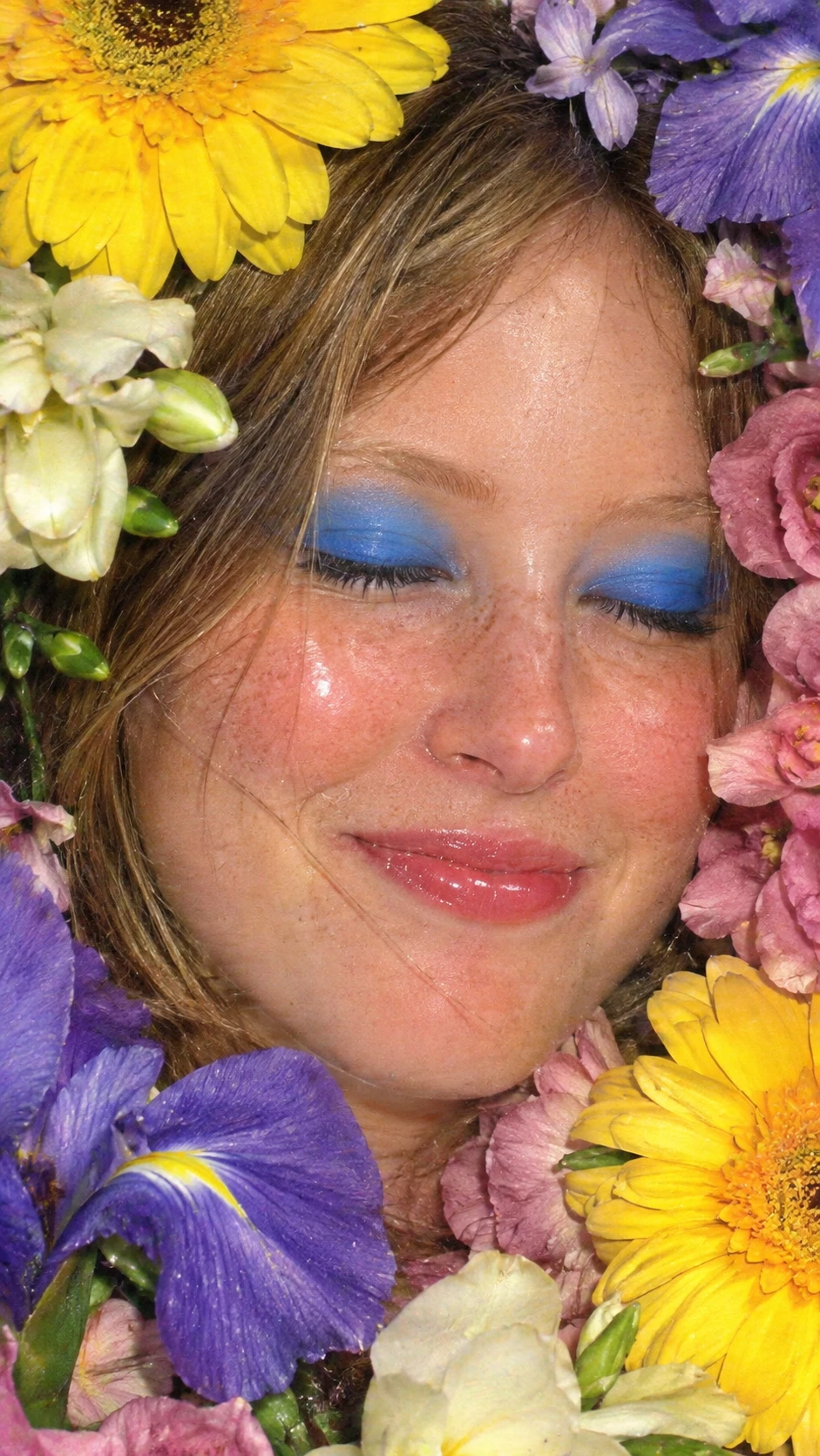 Uma jovem emoldurada por flores vibrantes e sombra azul ousada