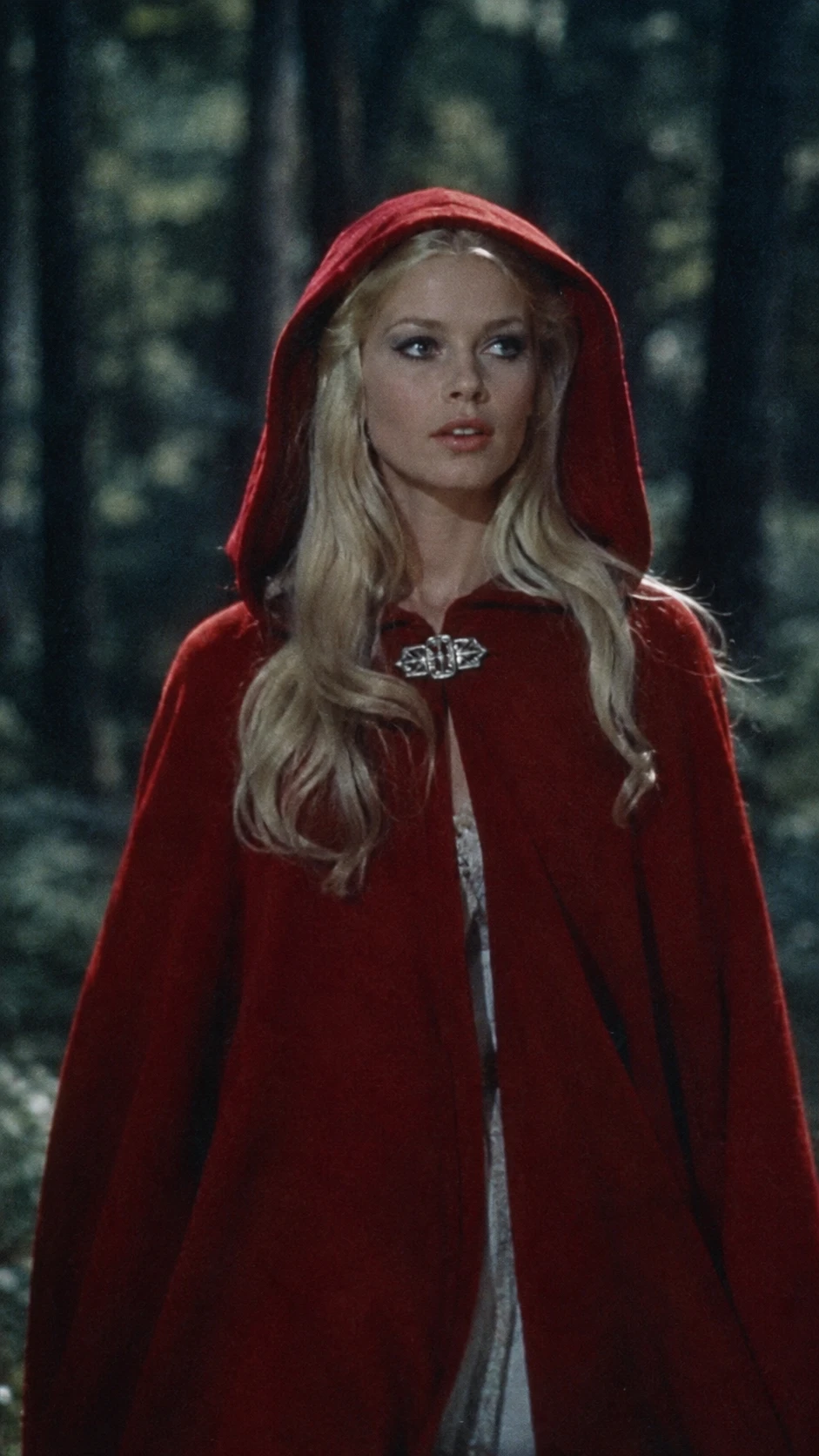 A young woman in a red hooded cloak walks through a dark forest