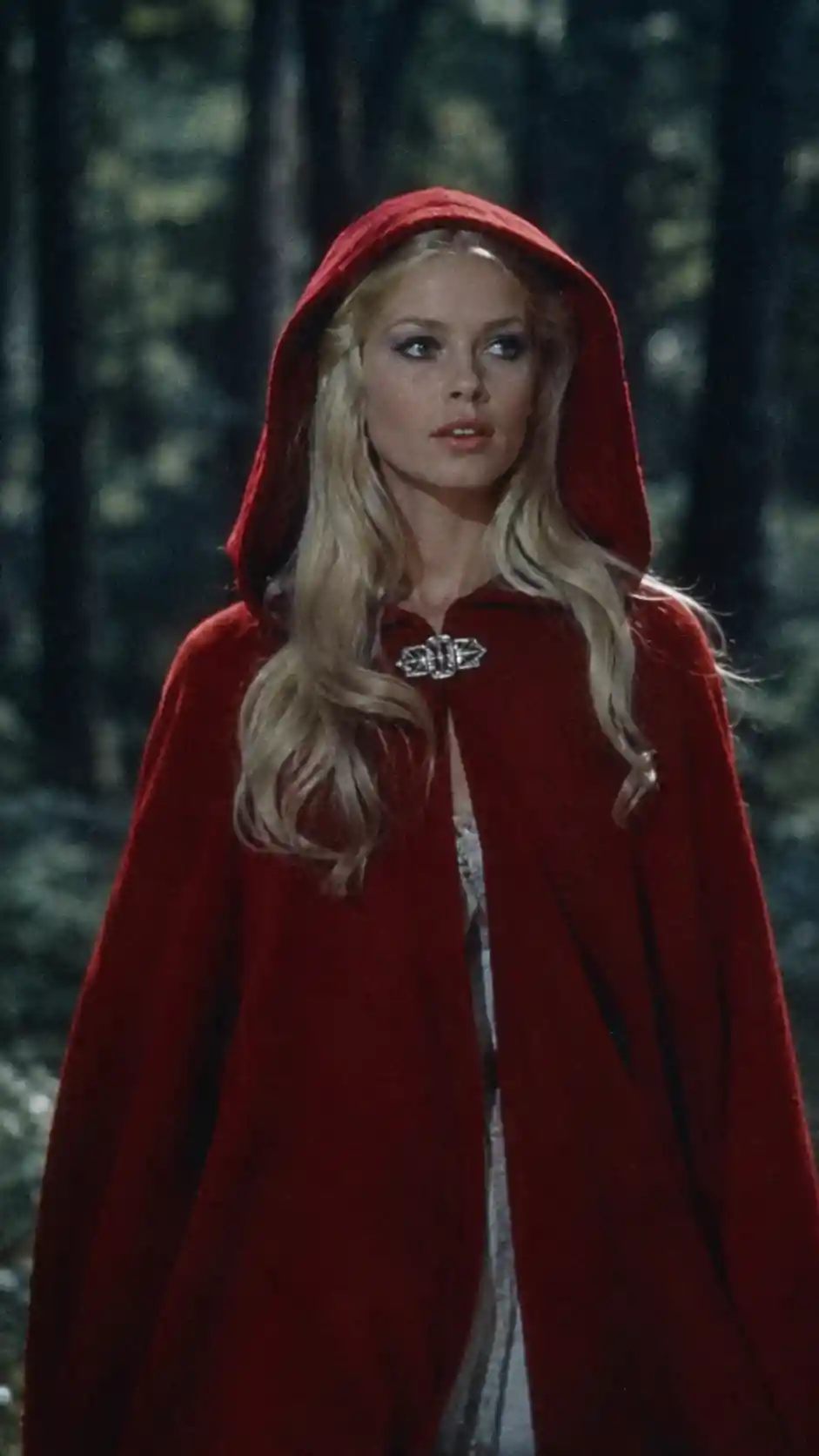 A young woman in a red hooded cloak walks through a dark forest