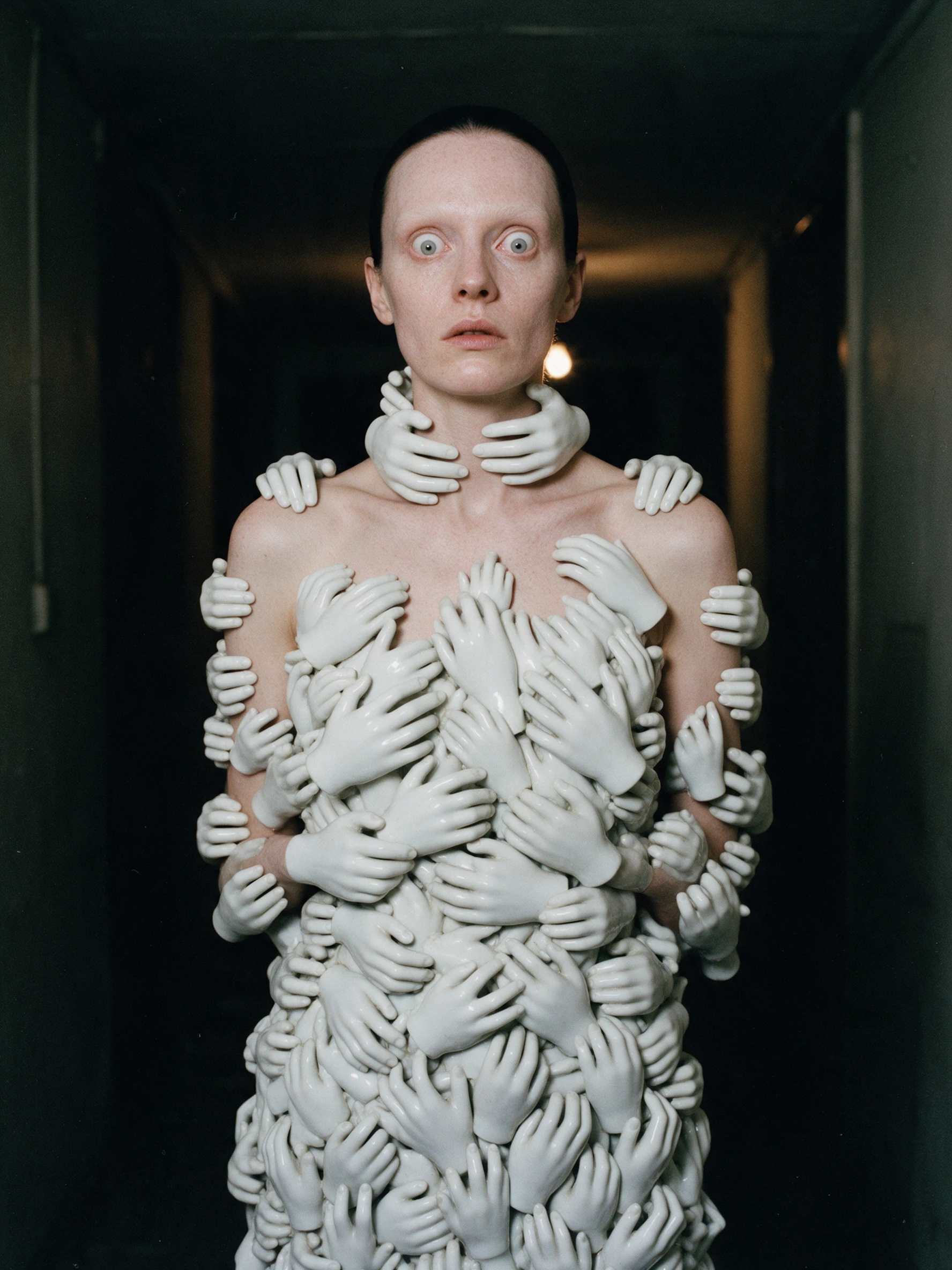 A fashion model frozen in a corridor wearing a gown of porcelain hands