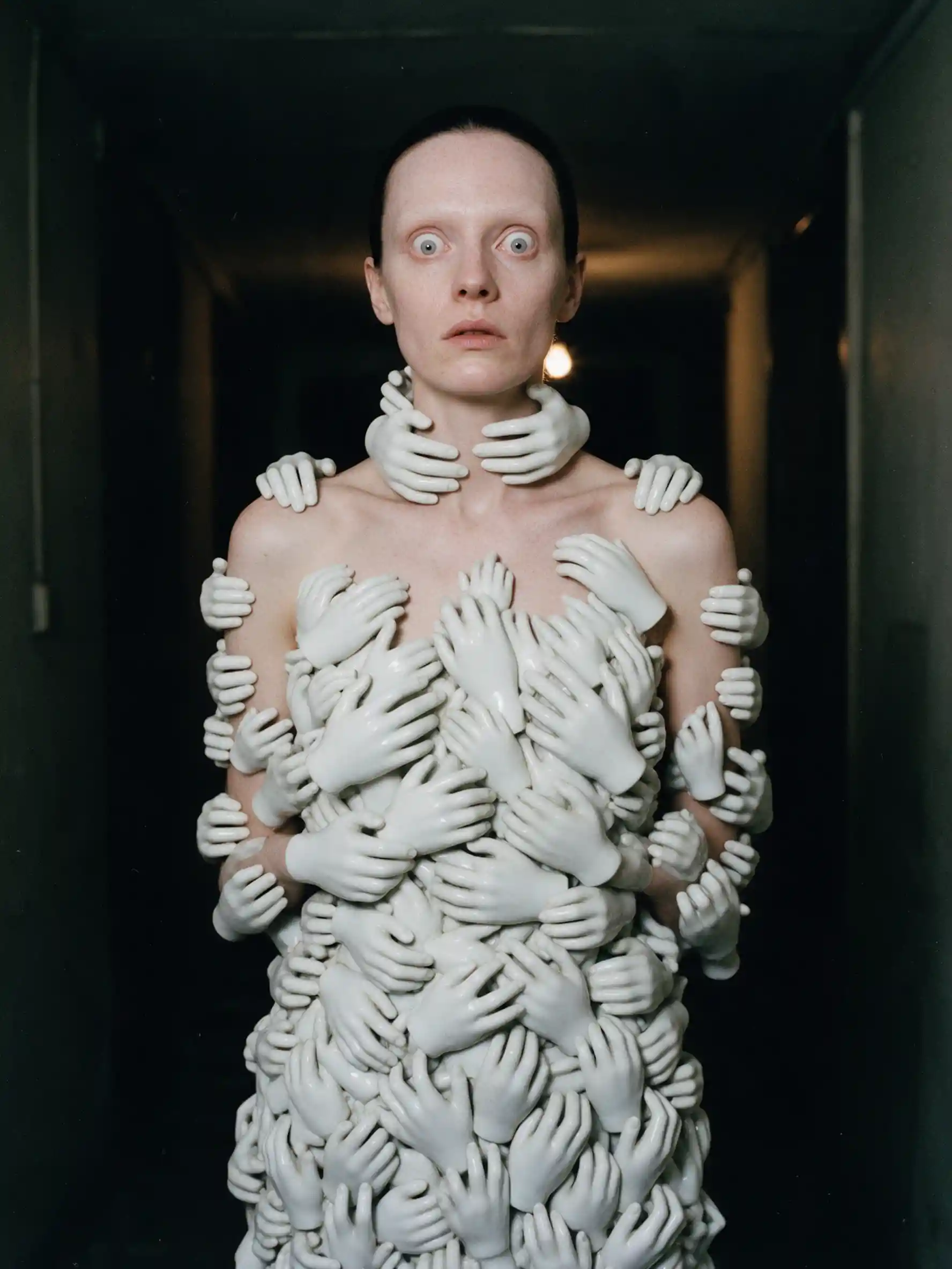 A fashion model frozen in a corridor wearing a gown of porcelain hands